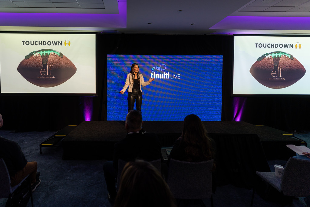 Kory Marchisotto on stage at Tinuiti Live with the television screens behind her showing that e.l.f. Cosmetics scored a marketing touchdown at the Big Game