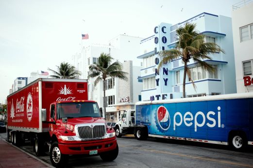 coke and pepsi trucks parked across from each other on street