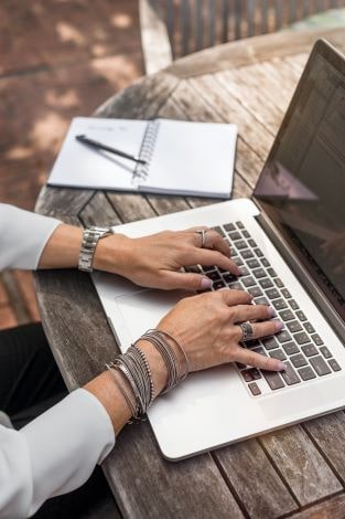 woman wearing silver jewelry typing on laptop focus on her hands