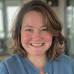 A woman smiling with short curly hair and a blue shirt.
