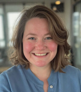 A woman smiling with short curly hair and a blue shirt.