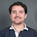 A man smiling with brown hair and a collared shit.