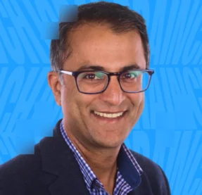 man in glasses smiling in front of blue background